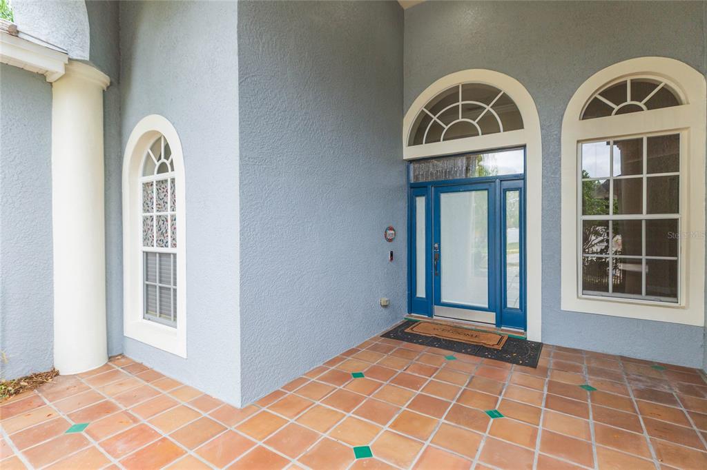 A covered entryway features blue doors, arched windows, and terracotta tile flooring with green accents — 4813 ARTESIAN ROAD, LAND O LAKES, FL