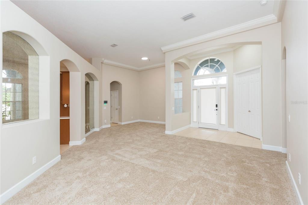 A carpeted living room features arched doorways, neutral walls, and a tiled entryway with a door — 4813 ARTESIAN ROAD, LAND O LAKES, FL
