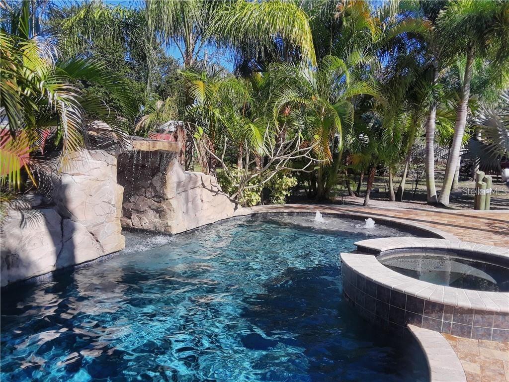 A swimming pool with a rock waterfall feature and an attached spa surrounded by palm trees — 681 JASMINE WAY S, ST PETERSBURG, FL