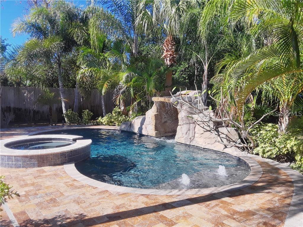 A backyard swimming pool features a rock waterfall, a raised spa, and surrounding palm trees — 681 JASMINE WAY S, ST PETERSBURG, FL