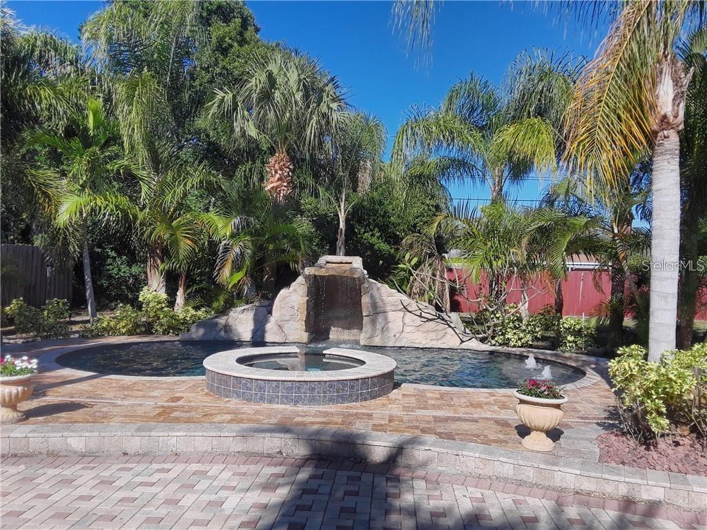 A backyard swimming pool features a rock waterfall, a raised spa, and surrounding palm trees — 681 JASMINE WAY S, ST PETERSBURG, FL