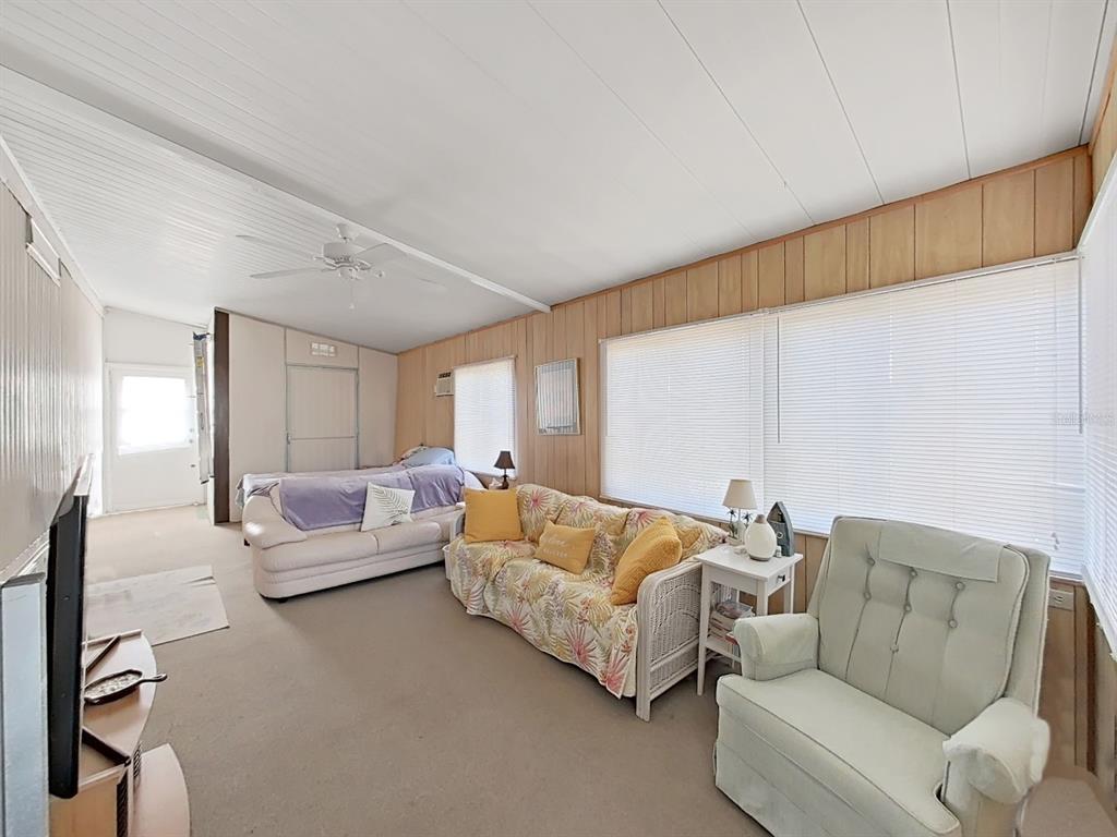 A living room features wood-paneled walls, a white ceiling, carpeted floors, and casual furniture — 12501 ULMERTON ROAD UNIT 140, LARGO, FL
