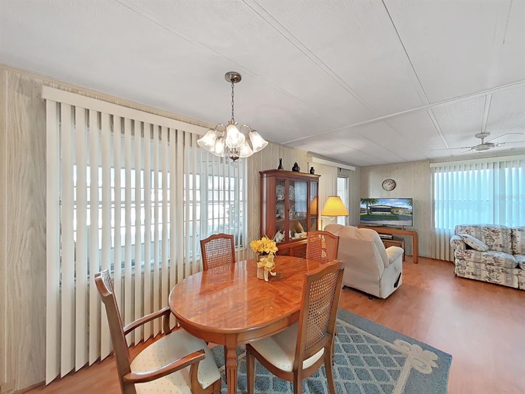 A dining area with a wooden table and chairs sits adjacent to a living room space — 12501 ULMERTON ROAD UNIT 140, LARGO, FL