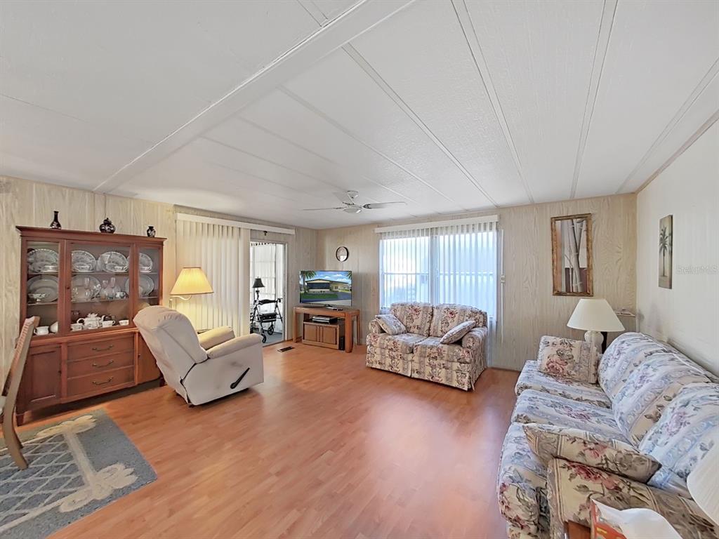 A living room features wood-look flooring, floral sofas, a recliner, and a wooden china cabinet — 12501 ULMERTON ROAD UNIT 140, LARGO, FL