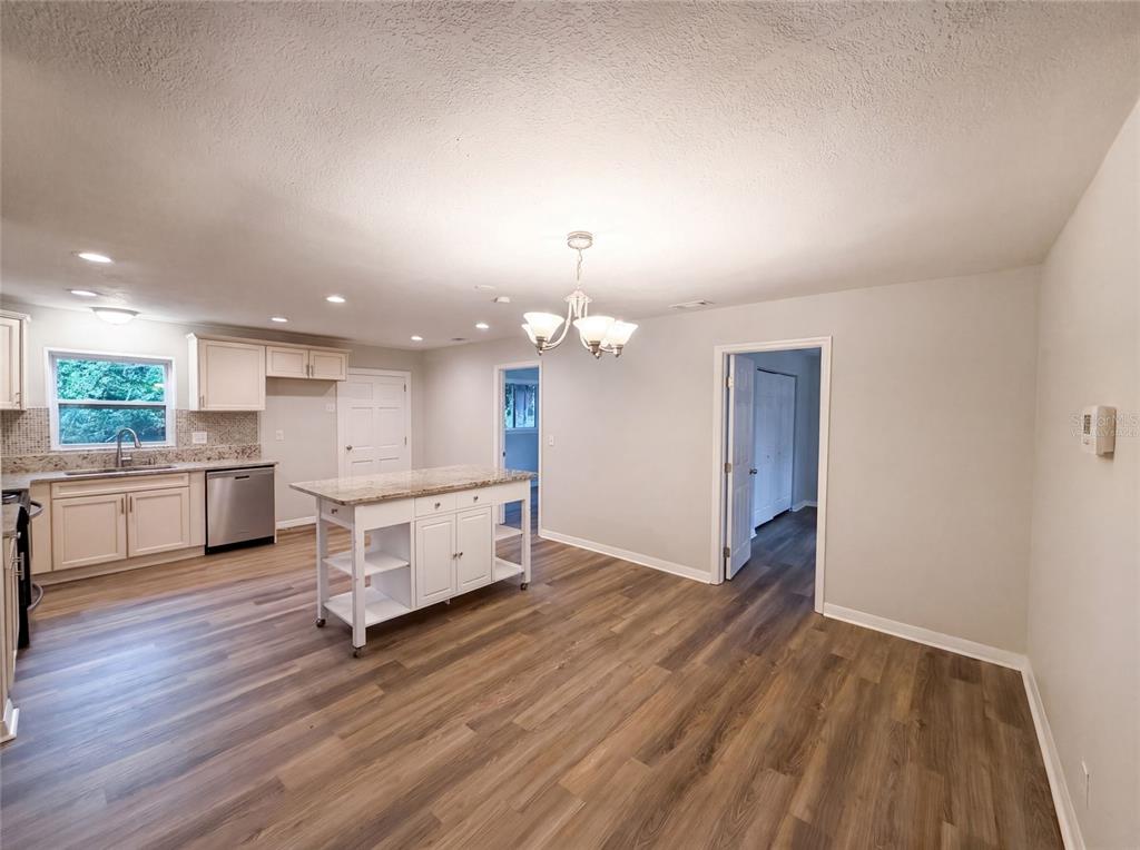 A kitchen and dining area with white cabinets, a granite island, and wood-look flooring — 13655 AUDREY LANE, LARGO, FL