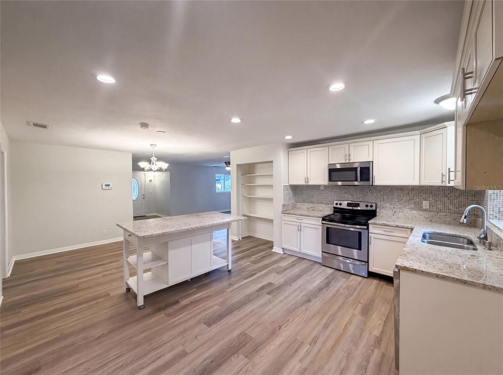 A kitchen features white cabinets, granite countertops, a mobile island, and wood-look flooring — 13655 AUDREY LANE, LARGO, FL