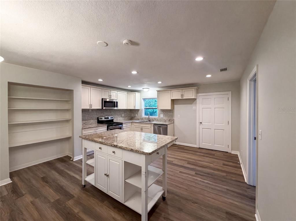 A kitchen features white cabinets, a granite-topped island, open shelving, and wood-look flooring — 13655 AUDREY LANE, LARGO, FL