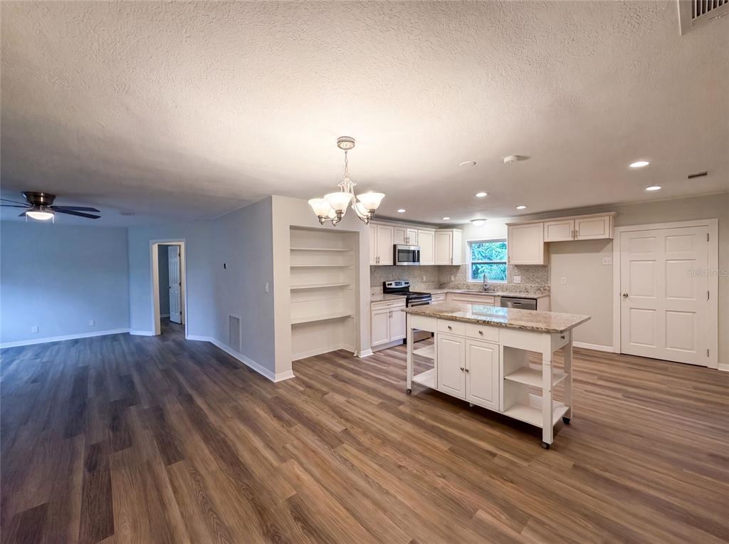 A kitchen with white cabinets, a granite-topped island, and wood-look flooring in an open space — 13655 AUDREY LANE, LARGO, FL