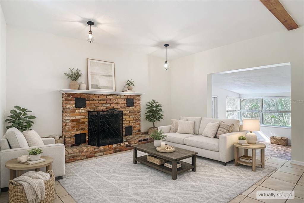 A living room features a brick fireplace, neutral furniture, and a large windowed sunroom beyond — 4621 JOHN MOORE ROAD, BRANDON, FL