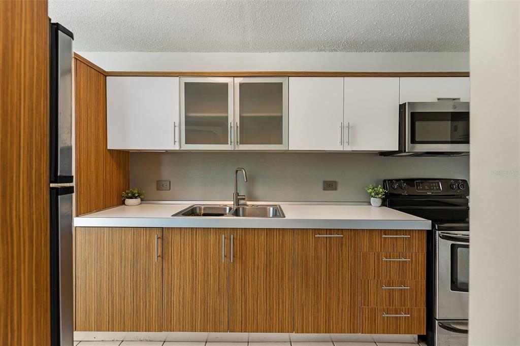 A kitchen features wood-grain lower cabinets, white upper cabinets, a stainless steel sink, and appliances — 37 COND ATRIUM PARK REGINA MEDINA Apt 408C, GUAYNABO, PR