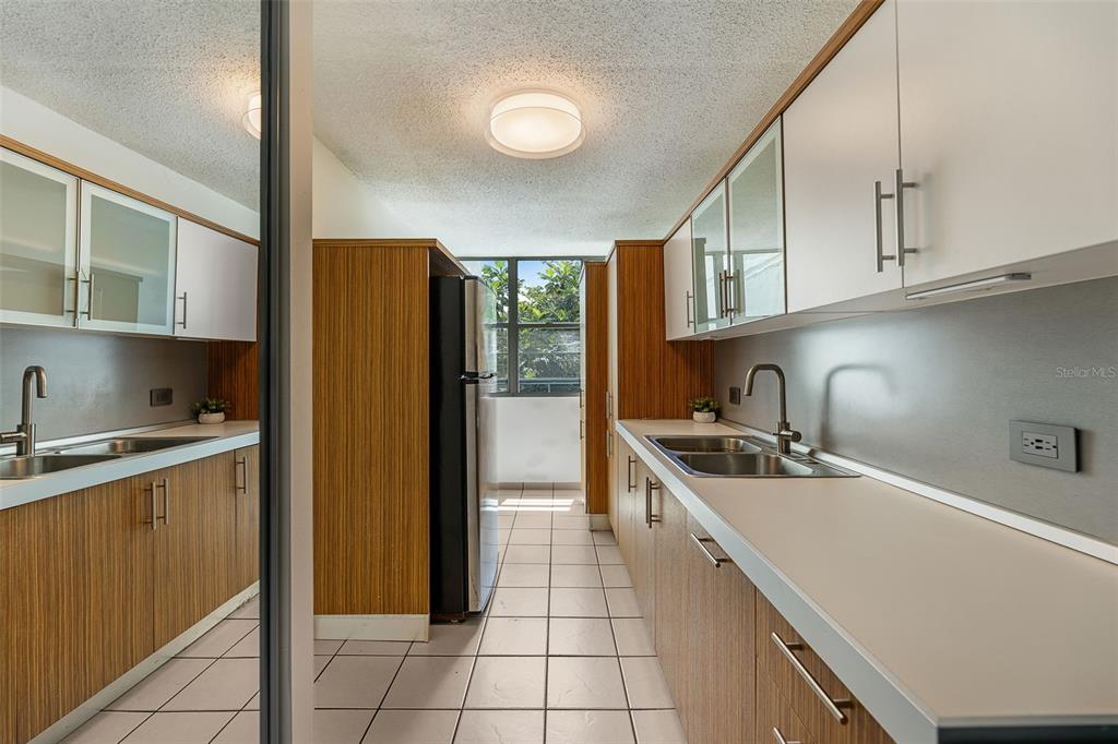 A galley kitchen features wood-grain lower cabinets, white upper cabinets, and light-colored tile flooring — 37 COND ATRIUM PARK REGINA MEDINA Apt 408C, GUAYNABO, PR