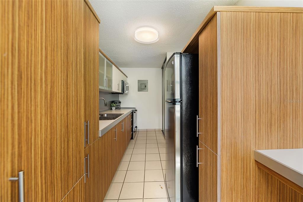A galley kitchen features wood-grain cabinets, stainless steel appliances, and light-colored floor tiles — 37 COND ATRIUM PARK REGINA MEDINA Apt 408C, GUAYNABO, PR