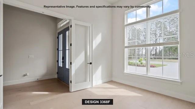 A bright room with light wood floors, a large window, and double glass-paneled doors — 19794 ROLLING RIDGE DRIVE, BROOKSVILLE, FL