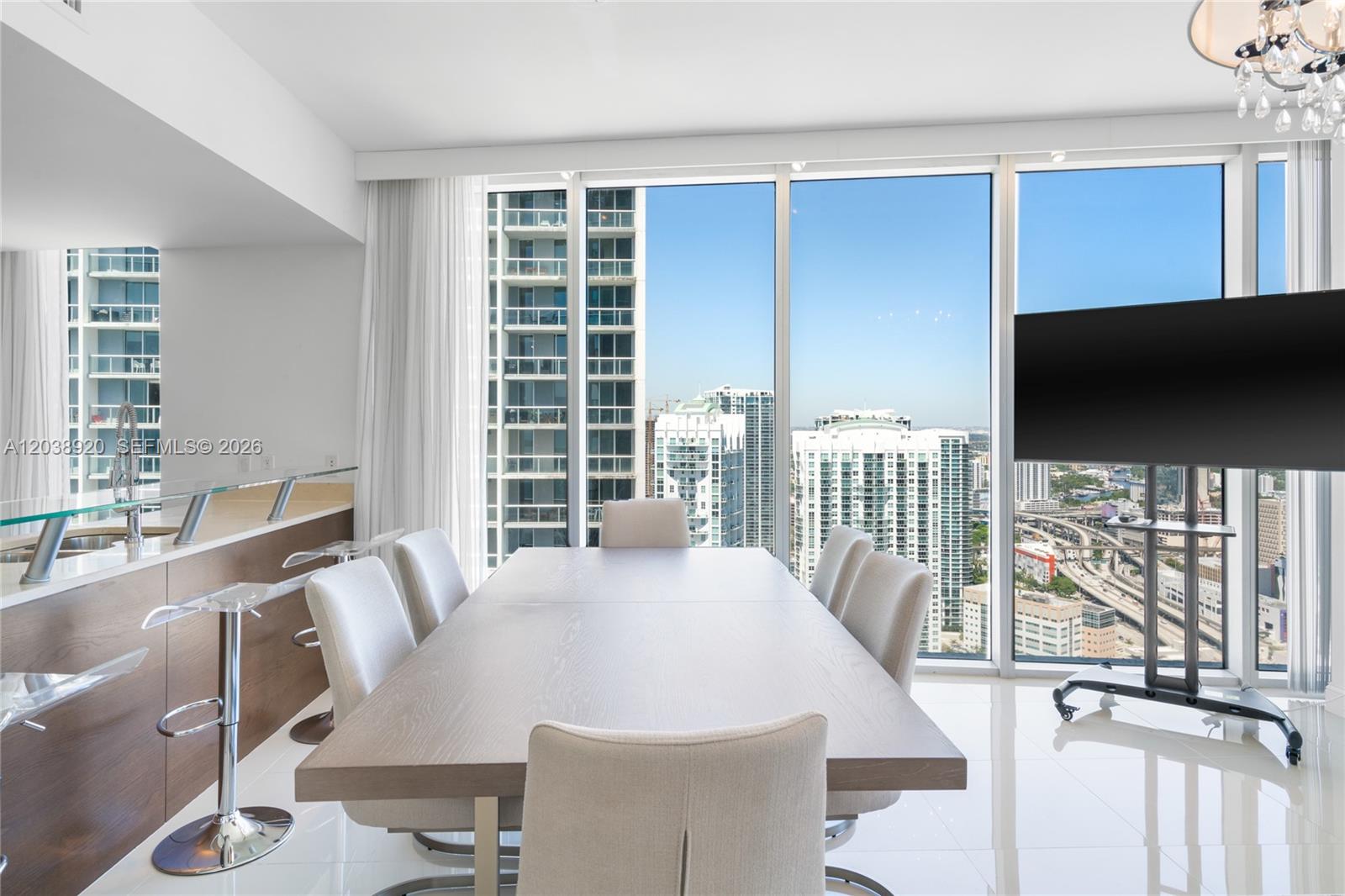 A dining room with a wooden table, chairs, and floor-to-ceiling windows overlooking a city — 475 Brickell Ave # 4315, Miami FL 33131, MIAMI, FL