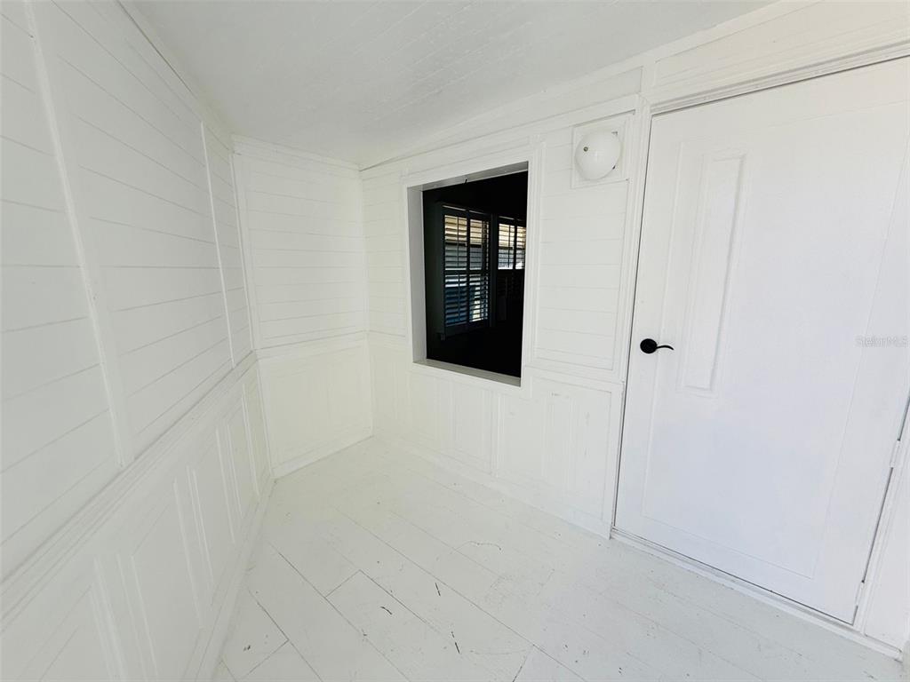 A small, white-painted room features paneled walls, a single window, and a closed door — 4851 W GANDY BOULEVARD UNIT B4L12, TAMPA, FL