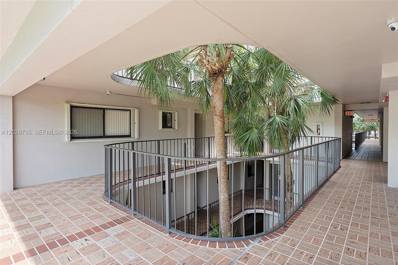 An open-air apartment building corridor features a central atrium with palm trees and metal railings — 8760 SW 133rd Ave Rd # 301, Miami FL 33183, MIAMI, FL