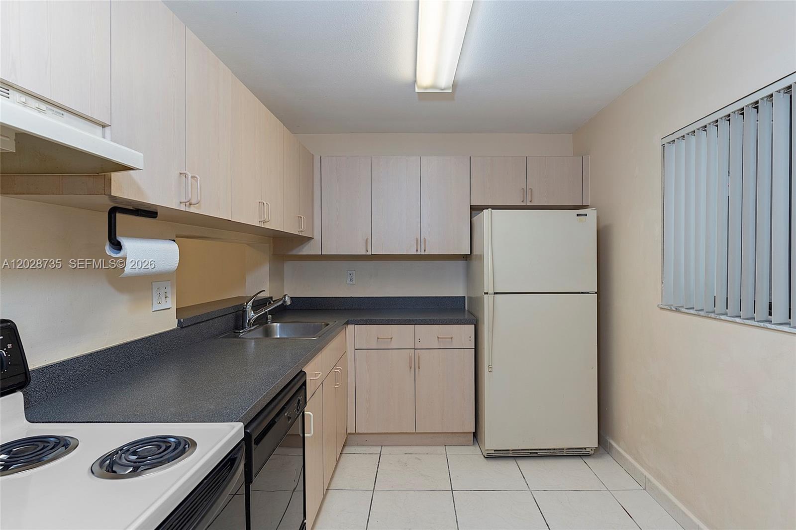 A kitchen features light wood cabinets, dark countertops, white appliances, and white tile flooring — 8760 SW 133rd Ave Rd # 301, Miami FL 33183, MIAMI, FL