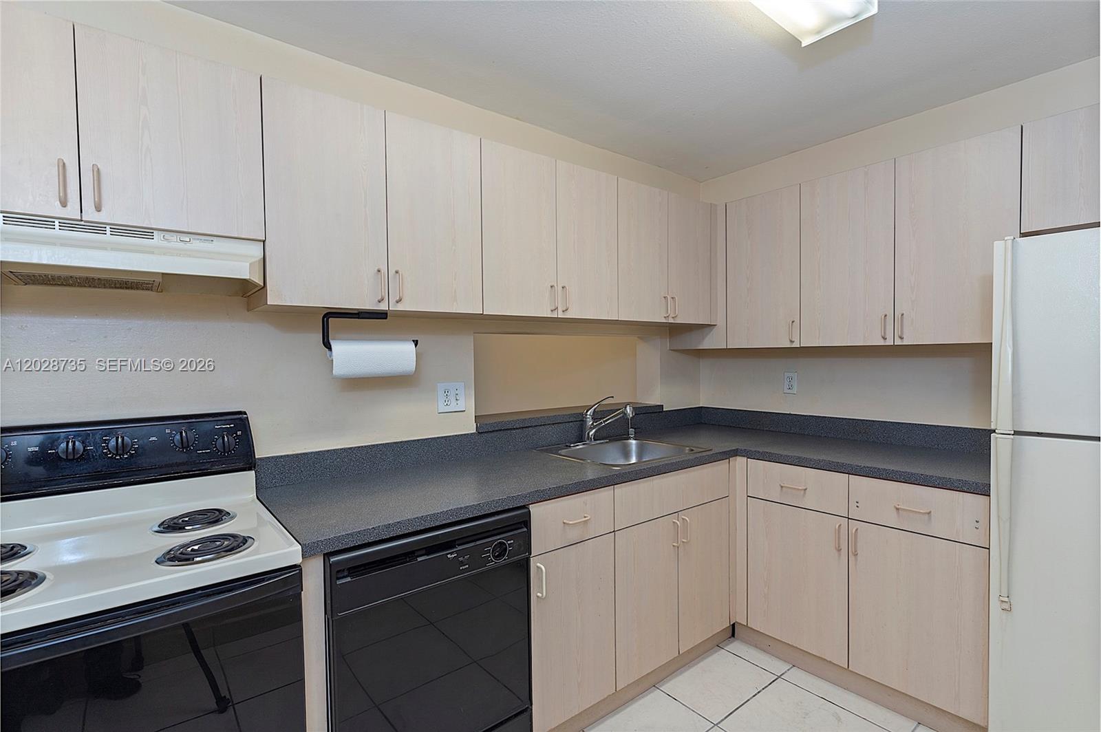 A kitchen features light wood cabinets, dark countertops, a black dishwasher, and white appliances — 8760 SW 133rd Ave Rd # 301, Miami FL 33183, MIAMI, FL