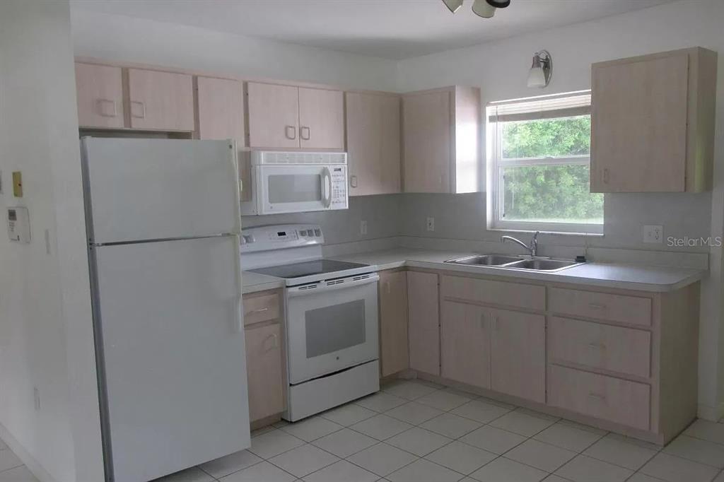 A kitchen features white appliances, light wood cabinets, tiled floors, and a window above the sink — 2911 BENTLEY STREET, SARASOTA, FL