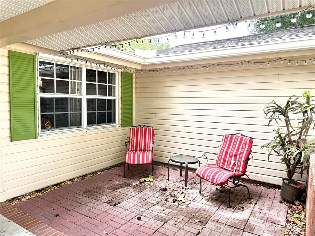 A patio with two red-striped chairs, a small table, and green shutters on the house — 12204 BEAR CREEK LANE, HUDSON, FL