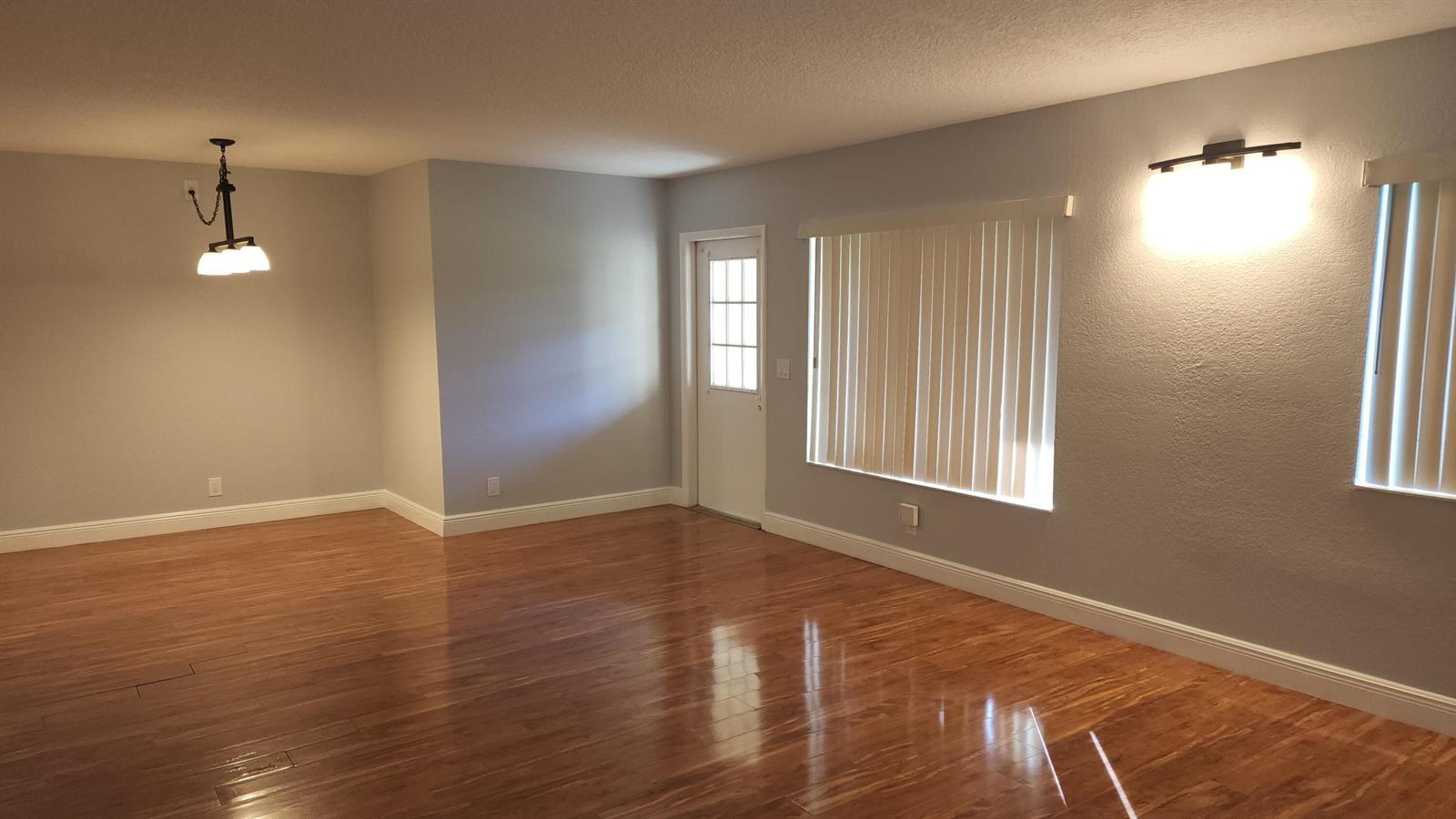 An empty room with hardwood floors, a hanging light fixture, and vertical window blinds — 527 Shady Pine Way # C1, FL 33415, FL