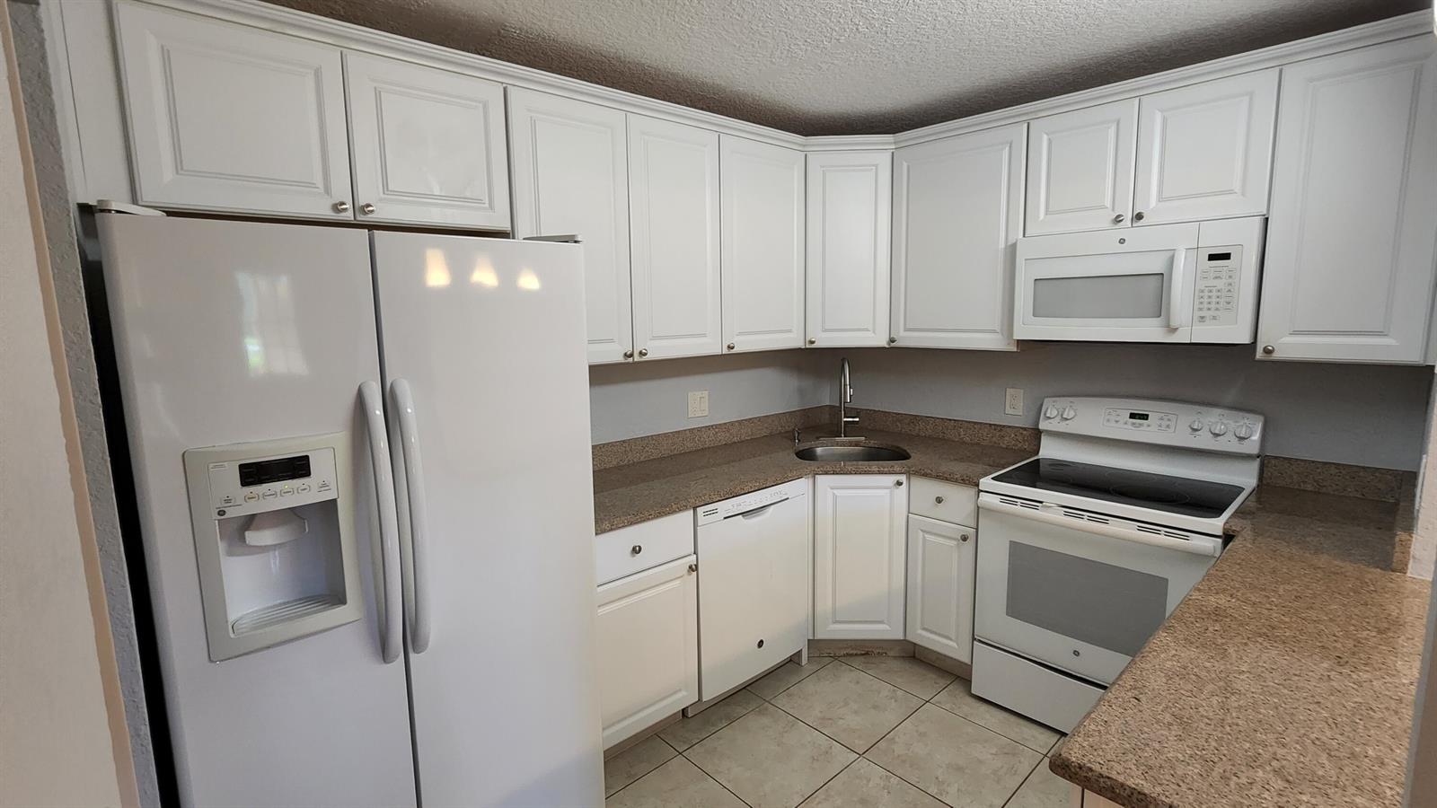 A kitchen features white cabinets, tan countertops, a white refrigerator, and a white stove — 527 Shady Pine Way # C1, FL 33415, FL