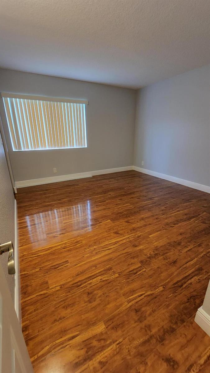 An empty room with light gray walls, white trim, and polished wood-look laminate flooring — 527 Shady Pine Way # C1, FL 33415, FL