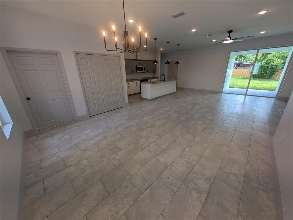 An open-concept living and kitchen area features tile flooring, a chandelier, and sliding glass doors — 1246 HERSCHELL STREET, LAKELAND, FL