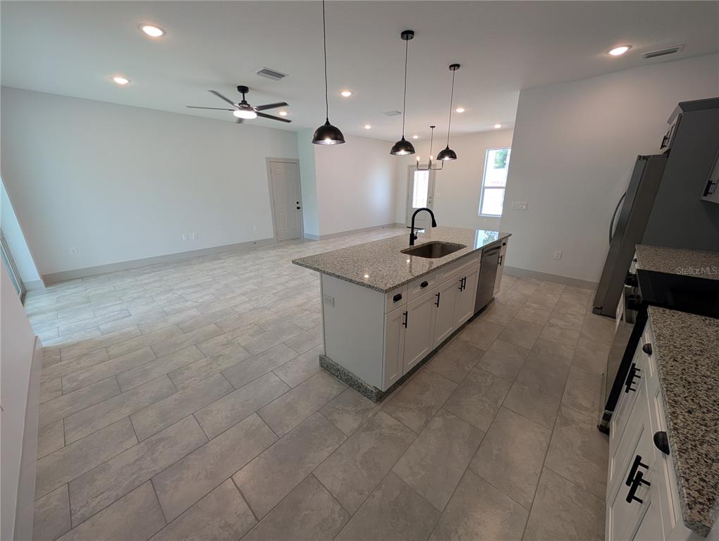 A modern kitchen features a granite-topped island, white cabinetry, and light gray tile flooring — 1246 HERSCHELL STREET, LAKELAND, FL