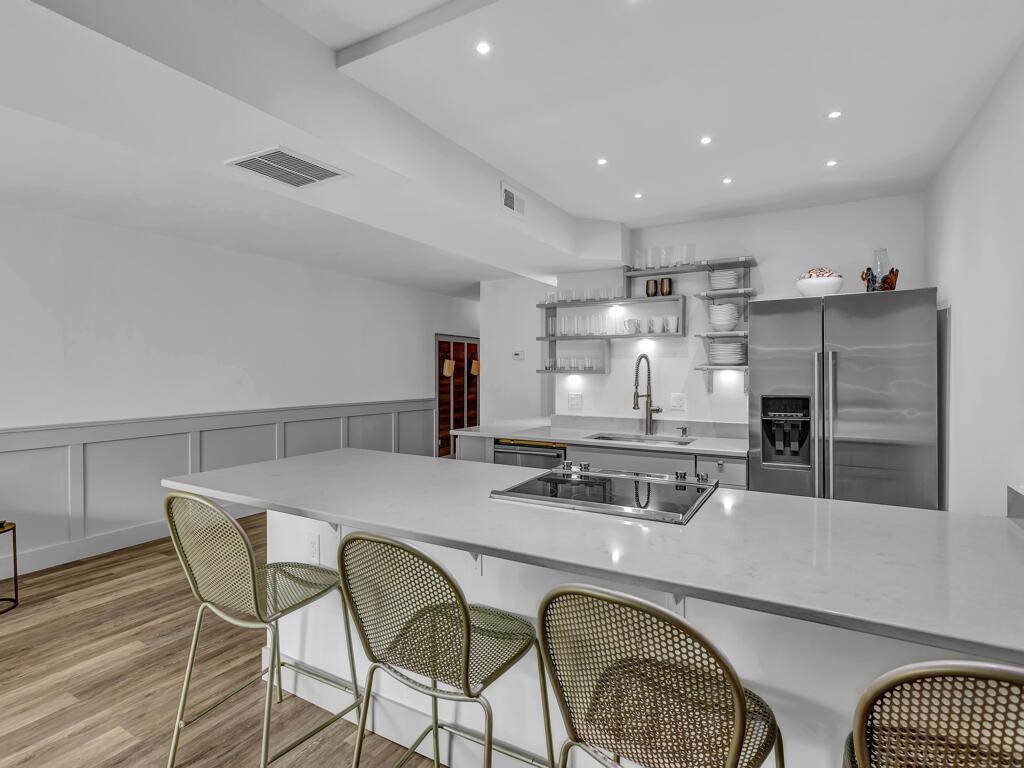 A modern kitchen features a white quartz island, stainless steel appliances, and gold metal barstools — 275 Date Palm Road # 304, Vero Beach FL 32963, VERO BEACH, FL