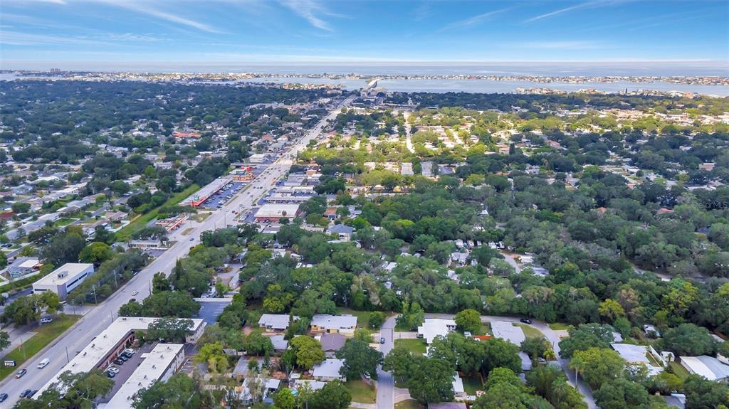 An aerial view shows a suburban neighborhood with a main road and distant coastal water — 1555 SHIRLEY PLACE, LARGO, FL