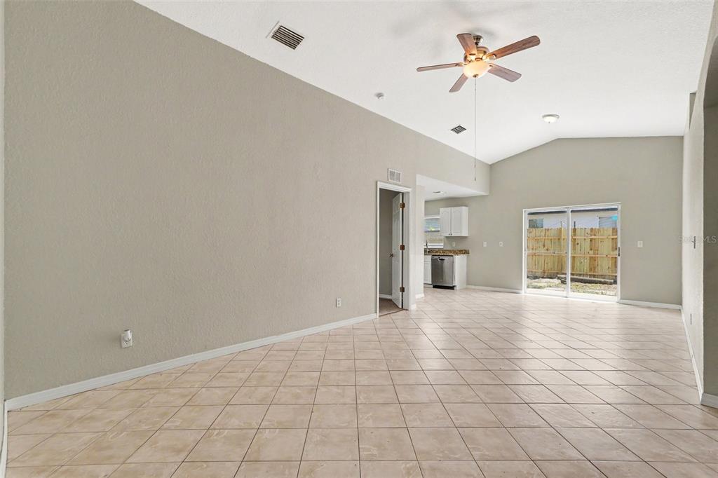 A spacious room with light-colored tile flooring, vaulted ceilings, a ceiling fan, and sliding doors — 1915 E MCBERRY STREET, TAMPA, FL