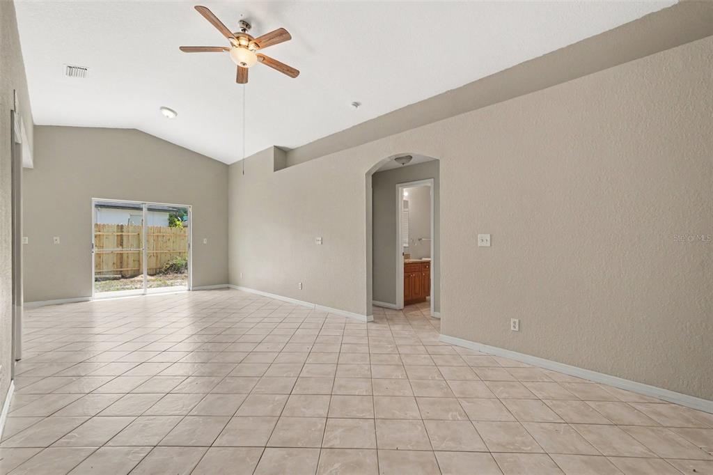 An empty room with beige tile flooring, vaulted ceilings, a ceiling fan, and sliding doors — 1915 E MCBERRY STREET, TAMPA, FL