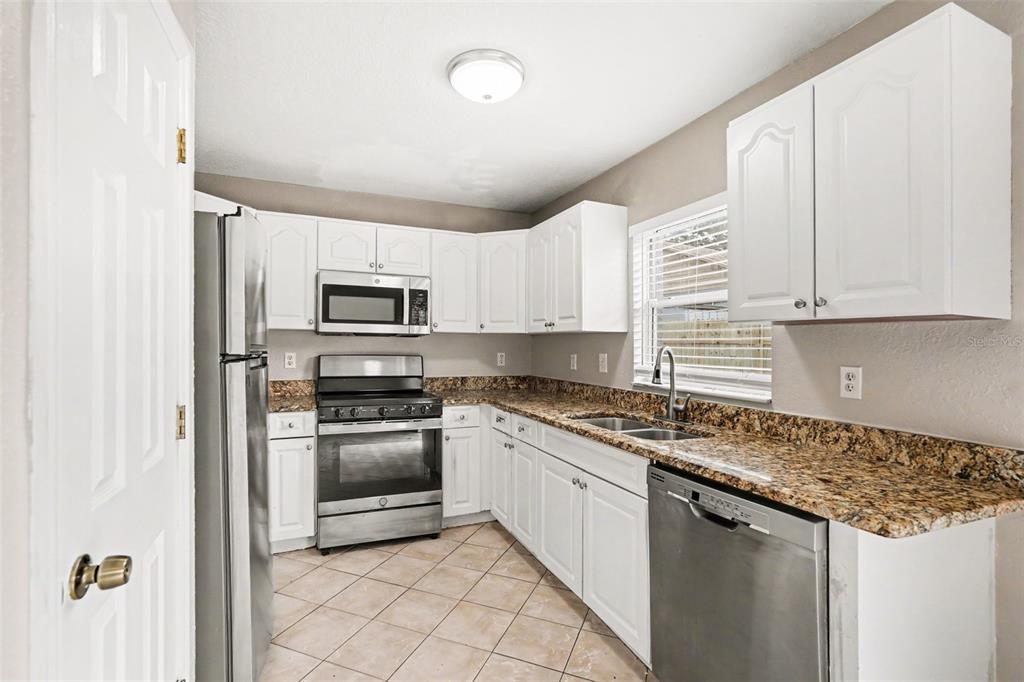 A kitchen features white cabinets, granite countertops, stainless steel appliances, and beige tile flooring — 1915 E MCBERRY STREET, TAMPA, FL