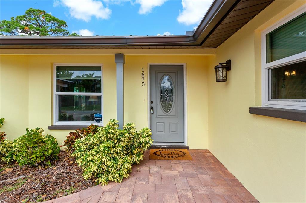 A pale yellow house exterior features a gray front door and a paved walkway — 1675 BLAKEMORE LANE, SARASOTA, FL