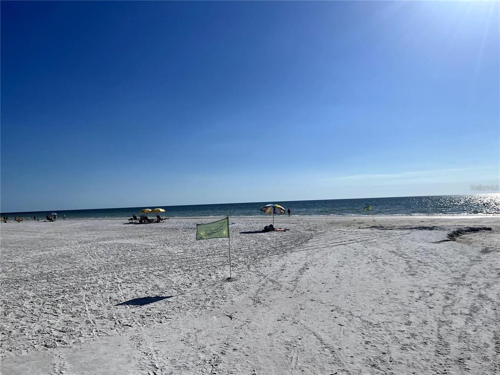 A wide, sandy beach with a green flag, beach umbrellas, and the ocean beyond — 1675 BLAKEMORE LANE, SARASOTA, FL