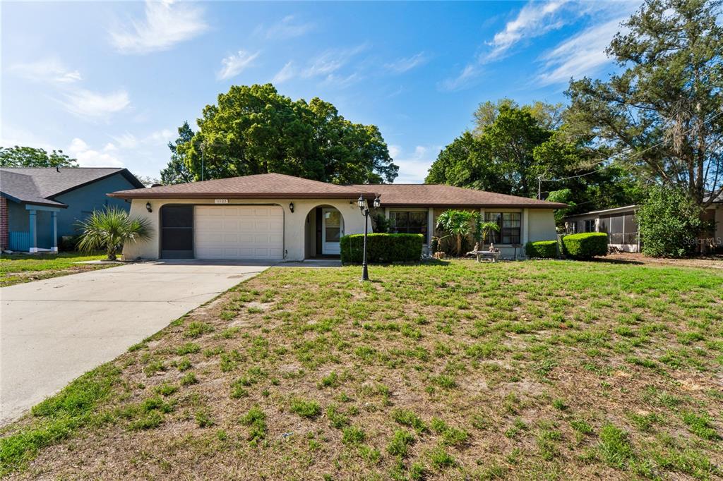 A single-story house with a beige exterior, a two-car garage, and a large front lawn — 11122 MADERIA STREET, SPRING HILL, FL