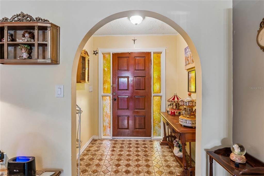 An arched entryway features a wooden front door with sidelights and patterned tile flooring — 11122 MADERIA STREET, SPRING HILL, FL