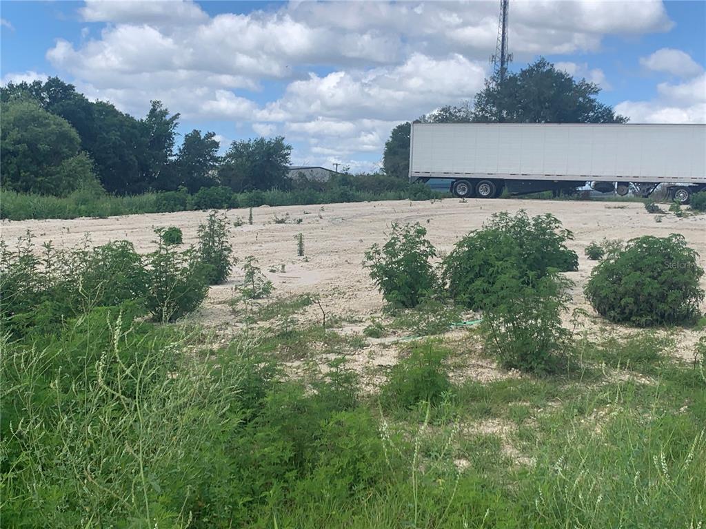 A large, flat, sandy lot features scattered green shrubs with a semi-trailer parked in the background — 0 RHINO ROAD, LAKELAND, FL