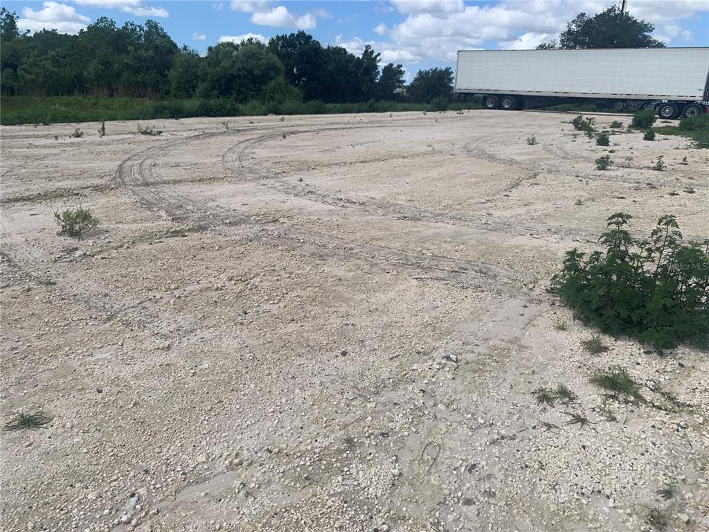 A large, unpaved dirt lot features tire tracks and a parked semi-trailer in the background — 0 RHINO ROAD, LAKELAND, FL