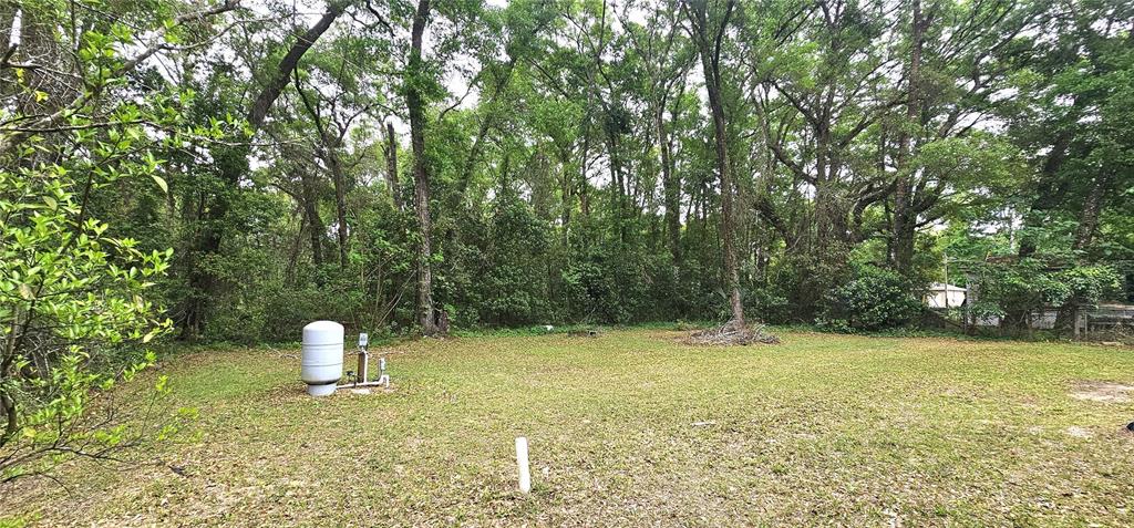 A grassy lot features a well tank and plumbing pipes against a backdrop of trees — 6605 NW 60TH COURT, OCALA, FL