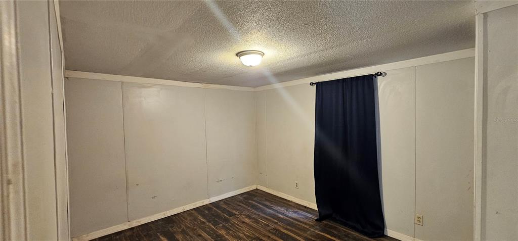 An empty bedroom features light-colored paneled walls, a dark curtain, and wood-look flooring — 6605 NW 60TH COURT, OCALA, FL