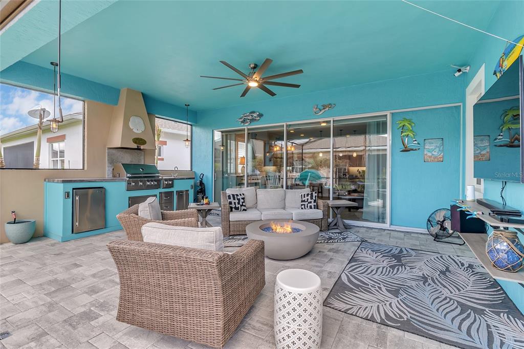 A covered outdoor patio features a kitchen, fire pit, wicker seating, and bright blue walls — 2764 GREENLANDS STREET, ST CLOUD, FL