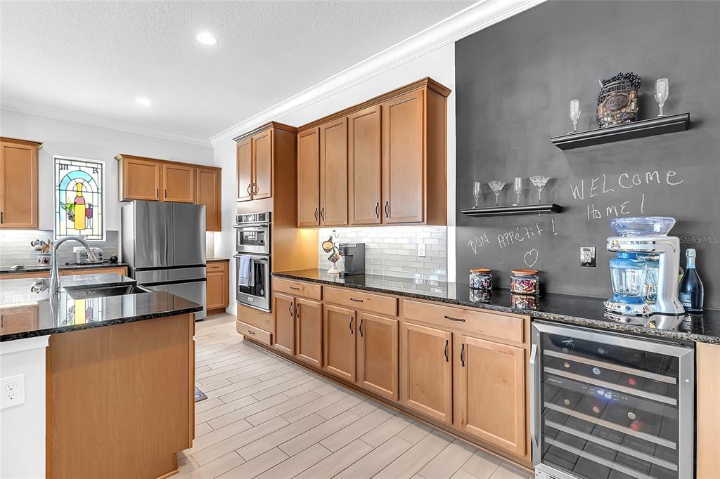 A kitchen features wood cabinets, dark granite countertops, stainless steel appliances, and a chalkboard wall — 2764 GREENLANDS STREET, ST CLOUD, FL