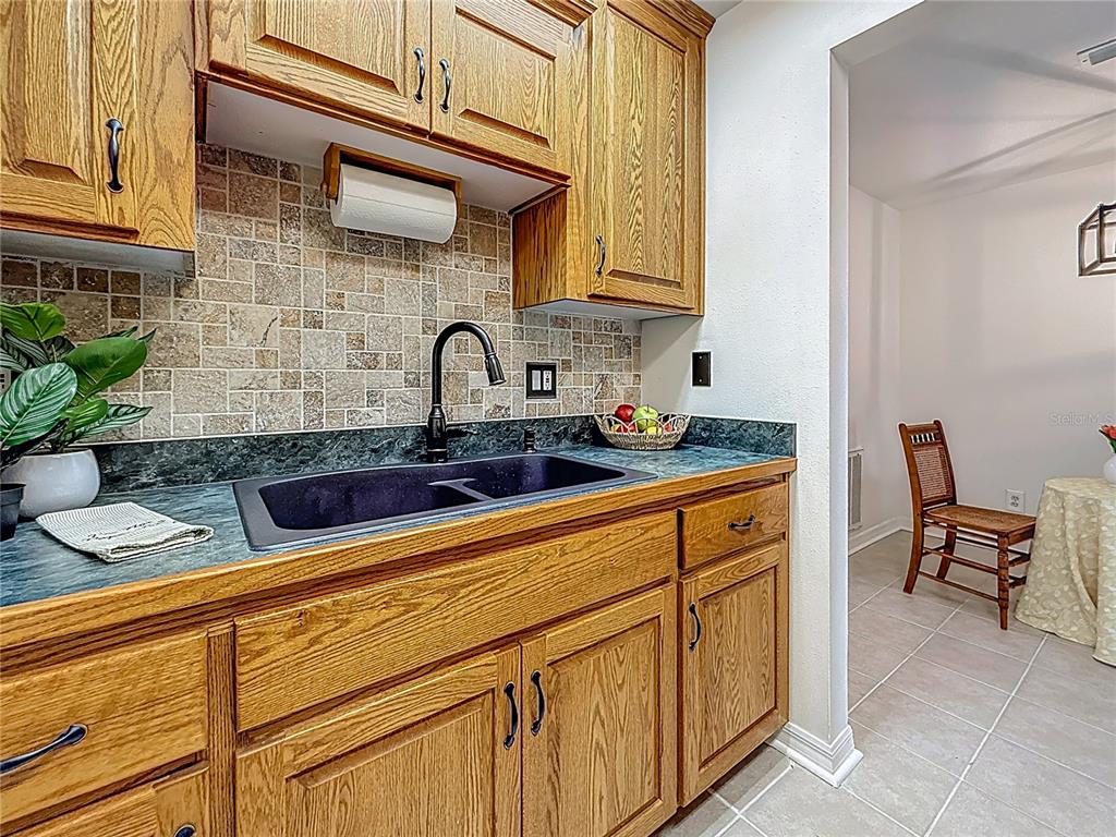 A kitchen features oak cabinets, a dark countertop, a black sink, and tiled backsplash — 2442 ENTERPRISE ROAD UNIT 6, CLEARWATER, FL