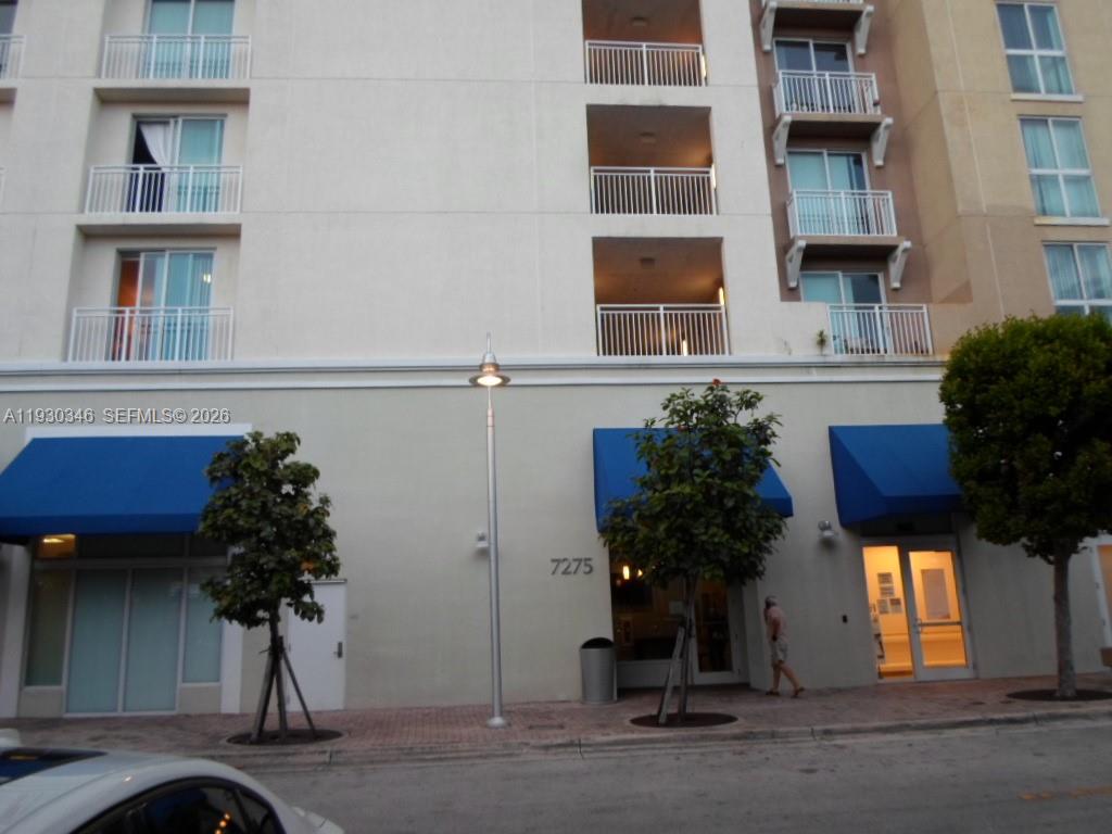 The exterior of a multi-story building features blue awnings, balconies, and a street-level entrance — 7275 SW 90th Way # 611, Miami FL 33156, MIAMI, FL