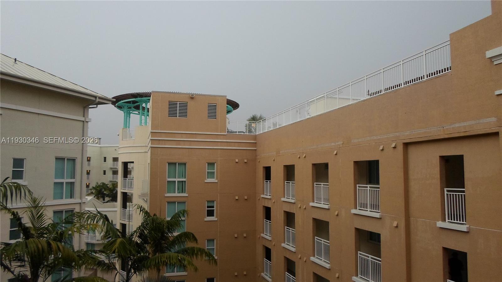 An exterior view of a multi-story tan building with balconies and a rooftop terrace — 7275 SW 90th Way # 611, Miami FL 33156, MIAMI, FL