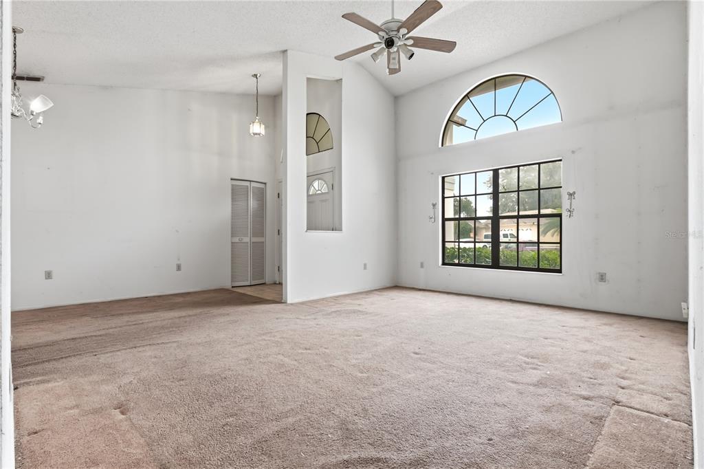 A spacious living room features vaulted ceilings, beige carpeting, a ceiling fan, and large windows — 9028 PAR COURT, HUDSON, FL