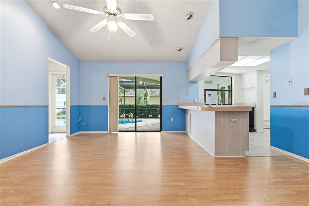 A room with light blue walls, wood-look flooring, a ceiling fan, and a kitchen pass-through — 9028 PAR COURT, HUDSON, FL