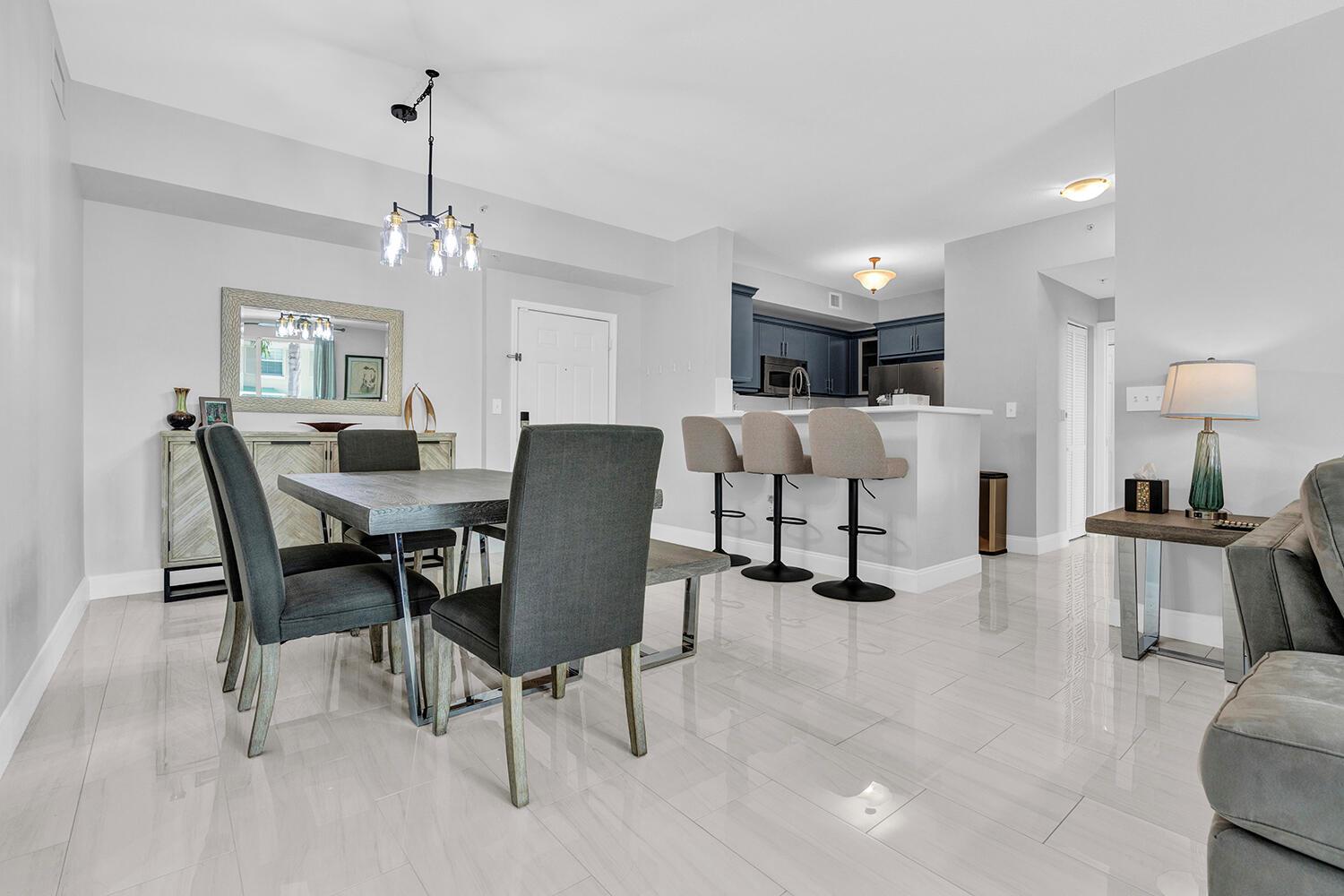 An open-concept dining area and kitchen with gray tile floors, dark chairs, and bar seating — 802 W Windward Way # 217, Lantana FL 33462, LANTANA, FL